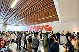 Config Registration Line with people waiting, Config rebranded logo in the center back wall behind the registration desks.