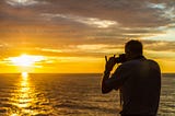 Man taking a photo with his camera. A beuatiful sunset in background.