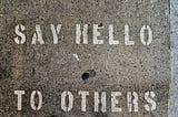 Bird’s eye view of the words “Say Hello to Others” spray-painted on a concrete sidewalk