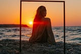 A woman on a beach at sunset, in front of a post and lintel frame, You are what you believe that you are.