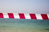 red and white access denied tape blocking off entry to a beautiful seascape