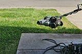 photo of lawn mower on patch of lawn next to driveway