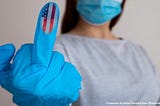 A person wearing mask giving the finger with American flag logo on fingertip
