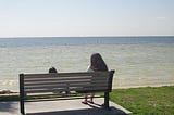 woman sitting on a bench overlooking the water while meditating.
