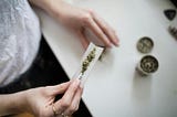 A hand holding a rolling paper with marijuana. The anonymous person is about to roll a joint.