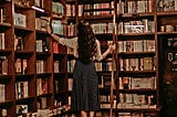 A woman in a library around thousands of books.