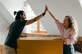 A Couple — man and woman — high fiving one another while moving a box