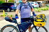 Man standing behind a bicycle loaded with bags and other gear.
