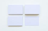 Four Stacks Of Plain Sized White Business Cards Against A White Background.