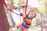 Image of a child on a swing, wearing a rainbow shirt, tutu and rainbow make-up