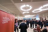 A photograph of people networking at an NLC event, with a banner in the foreground saying “National Leadership Centre”