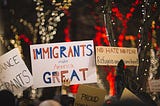 Protest signs at night. The signs read "imigrants make America great", "no hate no fear, refugees are welcome here" and "proud".