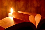 A candle shining behind a book with two centre leaves made into a heart.
