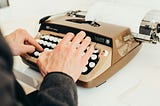 A person typing on a vintage typewriter, focusing on the keys of an old Galaxie Twelve model. The image evokes a sense of nostalgia, with the typewriter producing a typed sheet of paper in the background.