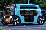 Light blue Zoox autonomous vehicle on road.
