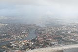 View of Porto through the fog from the airplane window. You can see River Douro, several bridges, and the red roofs of buildings.