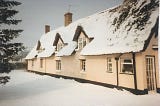 Thatched cottage with gable windows, traditional pink exterior, light covering of snow