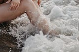 Woman with her legs in the ocean, at the beach.