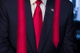 a person in a dark suit with a red tie, and the tie is very long