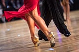 A woman in a red dress and a man in black pants, ballroom dancing.