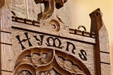 Color photo of the word Hymn carved in wood,  probably inside a church.