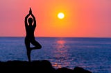 A woman practices yoga at sunrise on a beach