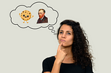 A woman with curly hair looking thoughtful, with a finger on her cheek and looking upwards. She is imagining a cartoonish cookie character alongside a portrait of Vincent Van Gogh, all contained within a thought bubble.