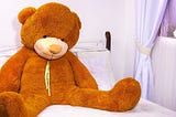 Lonely giant teddy bear sitting forgotten on a child bed | unwanted gift