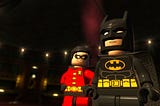 Lego Batman and Lego Robin stand next to each other. Batman is pondering his next movie while Robin grins goofily.