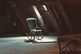 Rocking chair in a dusty attic beneath a window