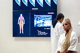 Photograph of a large doctor’s office with Mary J. Blige sitting in the foreground and body/breast imaging on the wall.