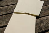 Two sheets of cream-coloured letter-writing paper on a wooden bench.