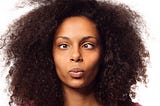 Dark-skinned woman with natural hairstyle on a white background, whose eyes present strabismus.