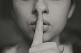 A woman holding a finger in front of her mouth to imply “silence”