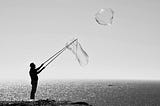 A man creating giant bubbles by the seaside