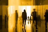 An artistic photograph of a silhouette of a person in a business suit walking in a company hallway.