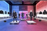 An AR Experience: Five mannequins are standing in a hall and on the sides jackets are floating on pedestals.