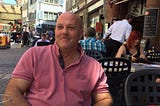 A photograph of Uncle Peter at a street cafe with buildings in the back