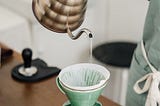 Barista pouring hot water through a funnel which has filter paper in it.