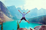 View from back of guy jumping above blue lake against mountains