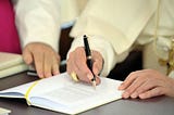 Pope Benedict signs a document with an ink pen.