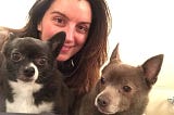 A photograph of Nicole DeCario, a woman with long brown hair, holding two small dogs.