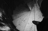 A top-down view of a spiral staircase with worn stone steps, partially illuminated