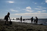 a photo of children and others scattered along the beach/ocean. they appear mostly as silhouettes, without distinguishing characteristics.