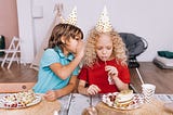 A young boy whispering to a young girl at a party.