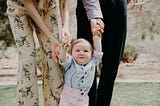 Toddler walking with his hands being held above his head by unseen parents