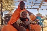 Adiza* mère de famille déplacée, assise avec son enfant sous un hangar.. Photo : PAM/ Aboubacar Sidibé