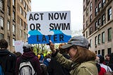 Protestor with sign that reads: “Act Now or Swim Later”