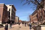 Brick buildings on the left and right, a handful of students walking down a pathway, and blue skies.