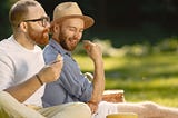 A romantic gay couple enjoying a picnic outside.